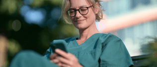 Pflegekraft schaut in der Pause zufrieden auf ihr Smartphone